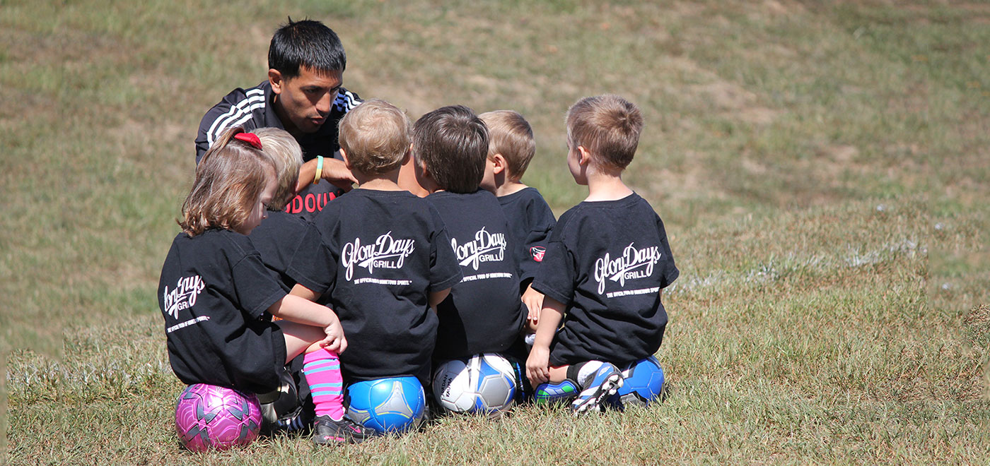Kids soccer coach huddling with team.